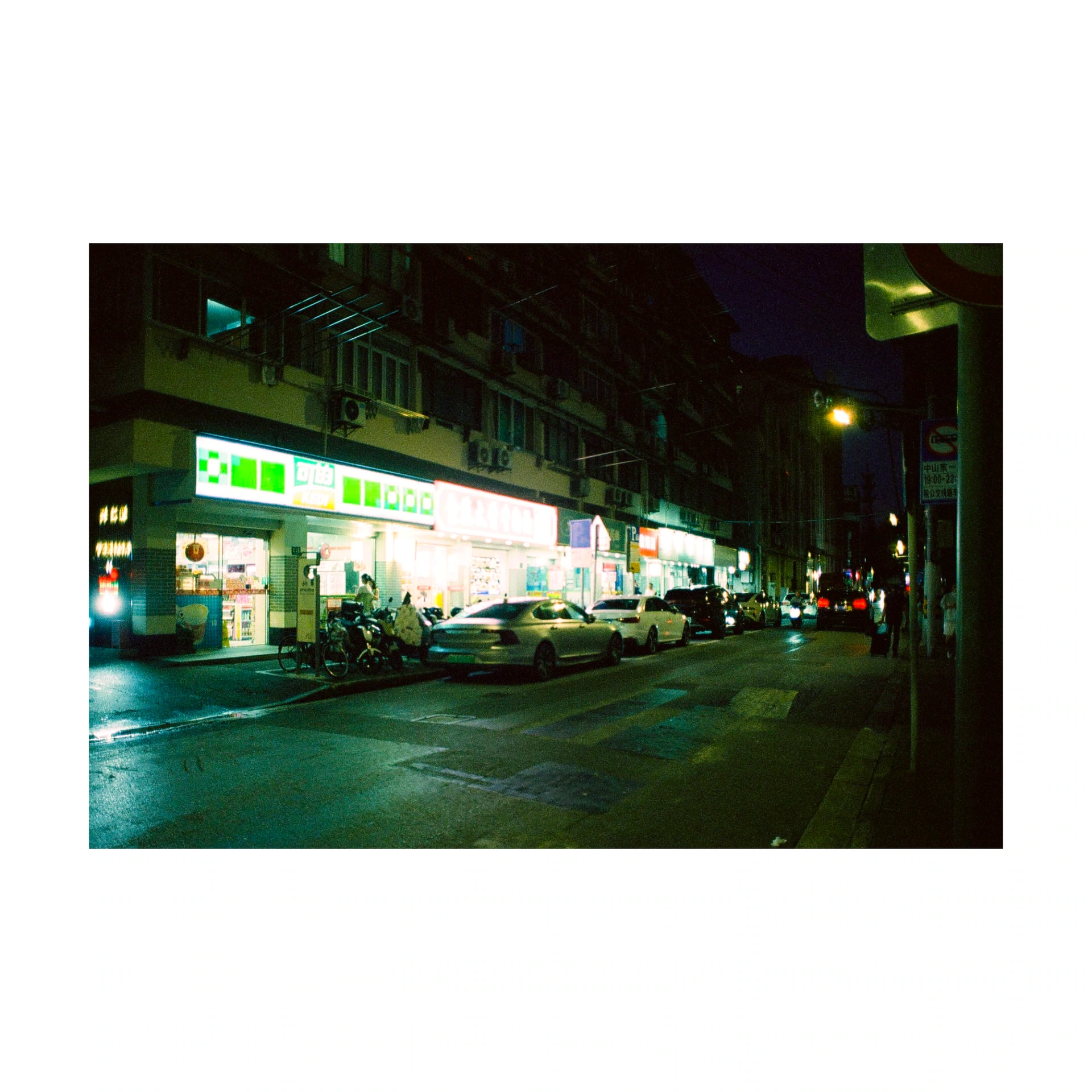 Night-time street lit by green and white shop signs