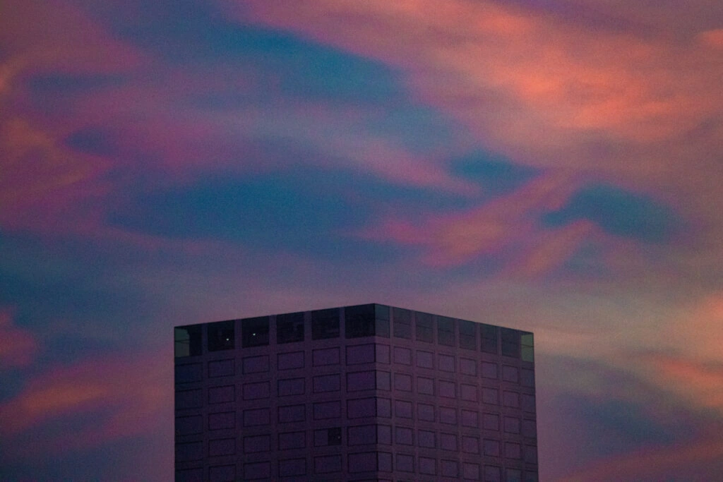 A dark building beneath pink and blue clouds