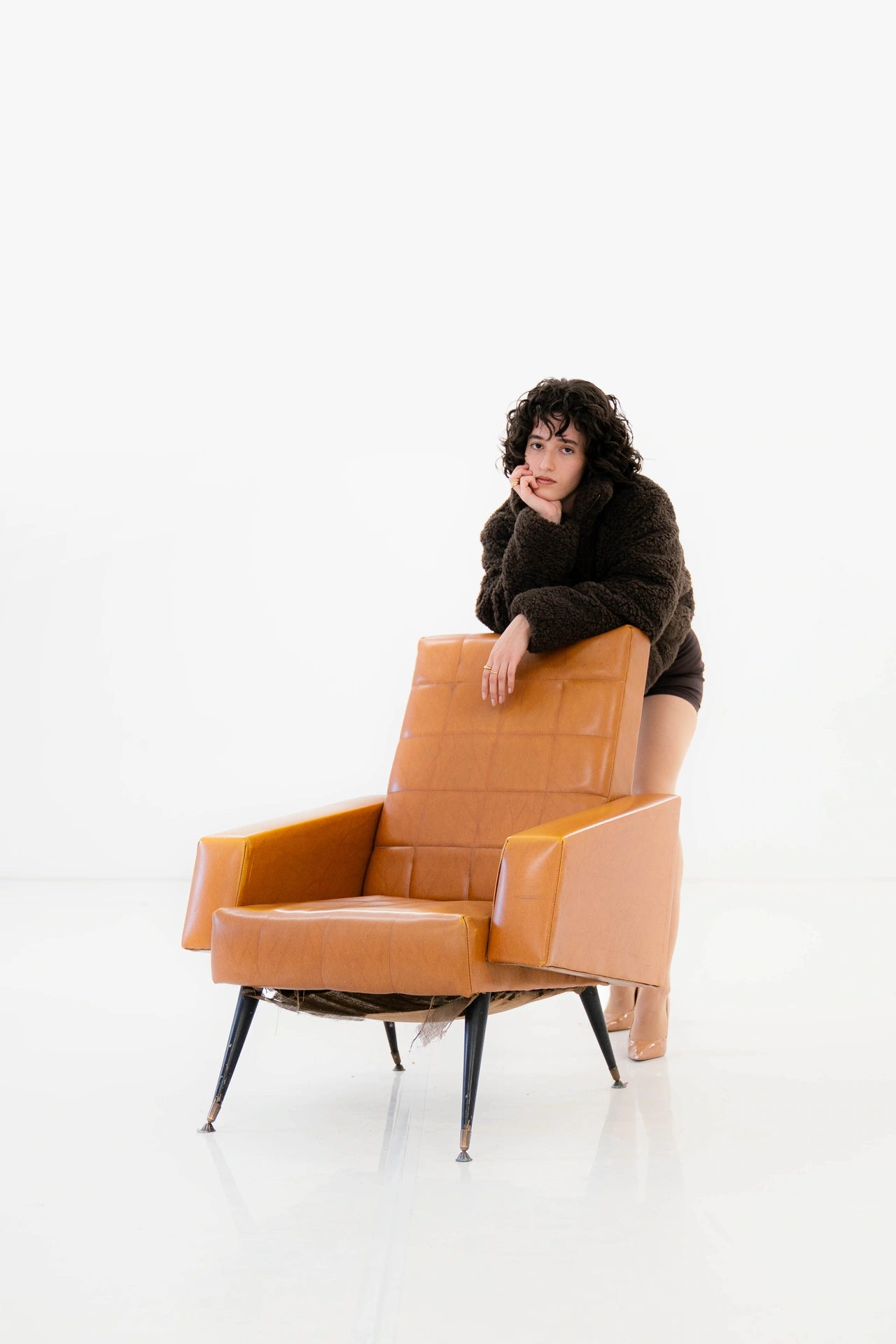 Diana debout derrière le dossier d’un fauteuil orange sur fond blanc