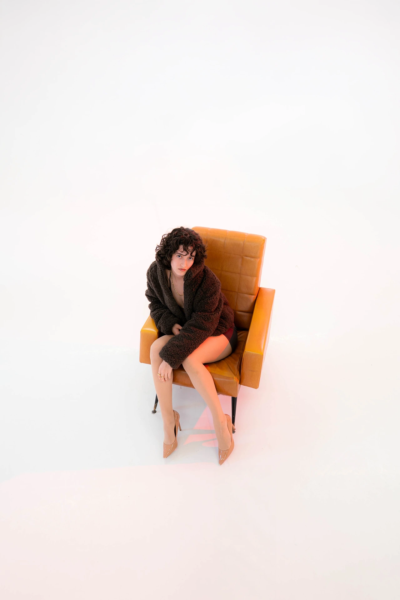 Diana assise dans un fauteuil orange au milieu d’un vaste fond blanc