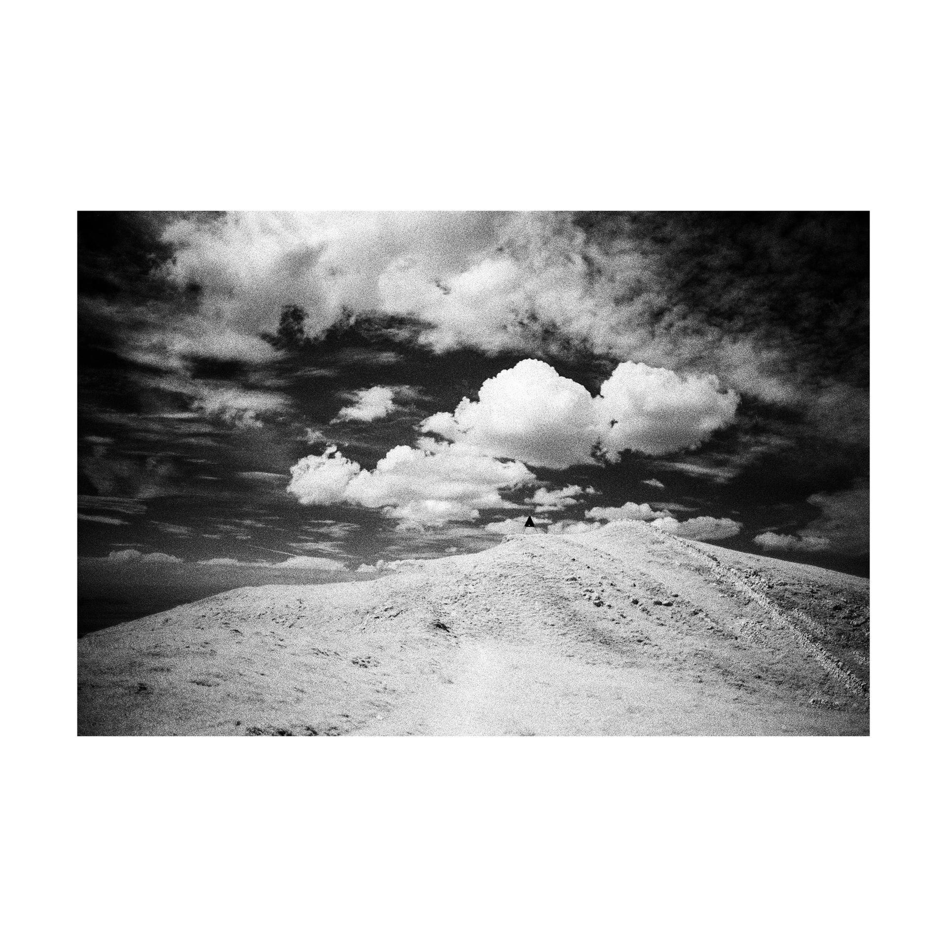 Black and white infrared landscape with a pale hill and dramatic clouds