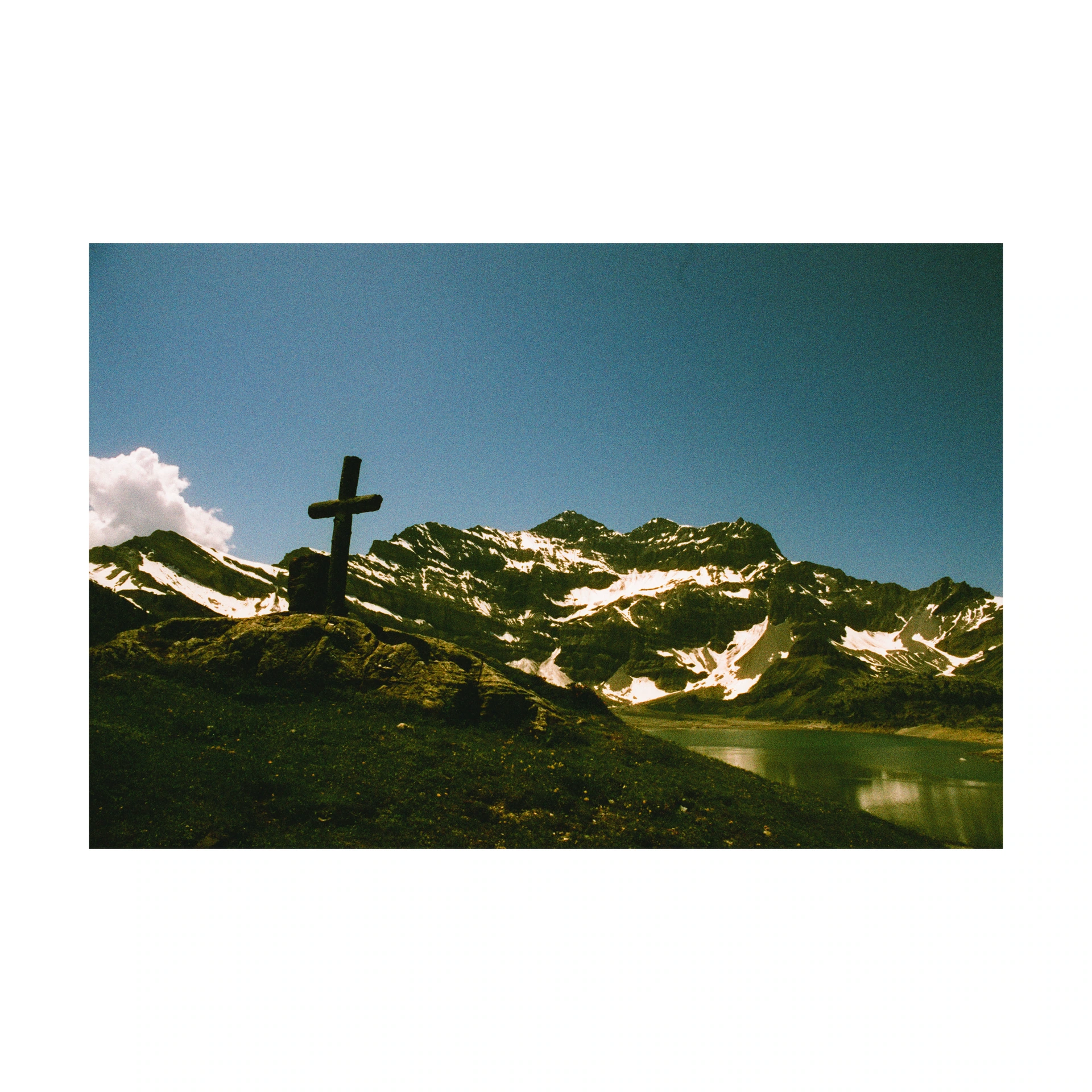 Cross beside a mountain lake under a blue sky