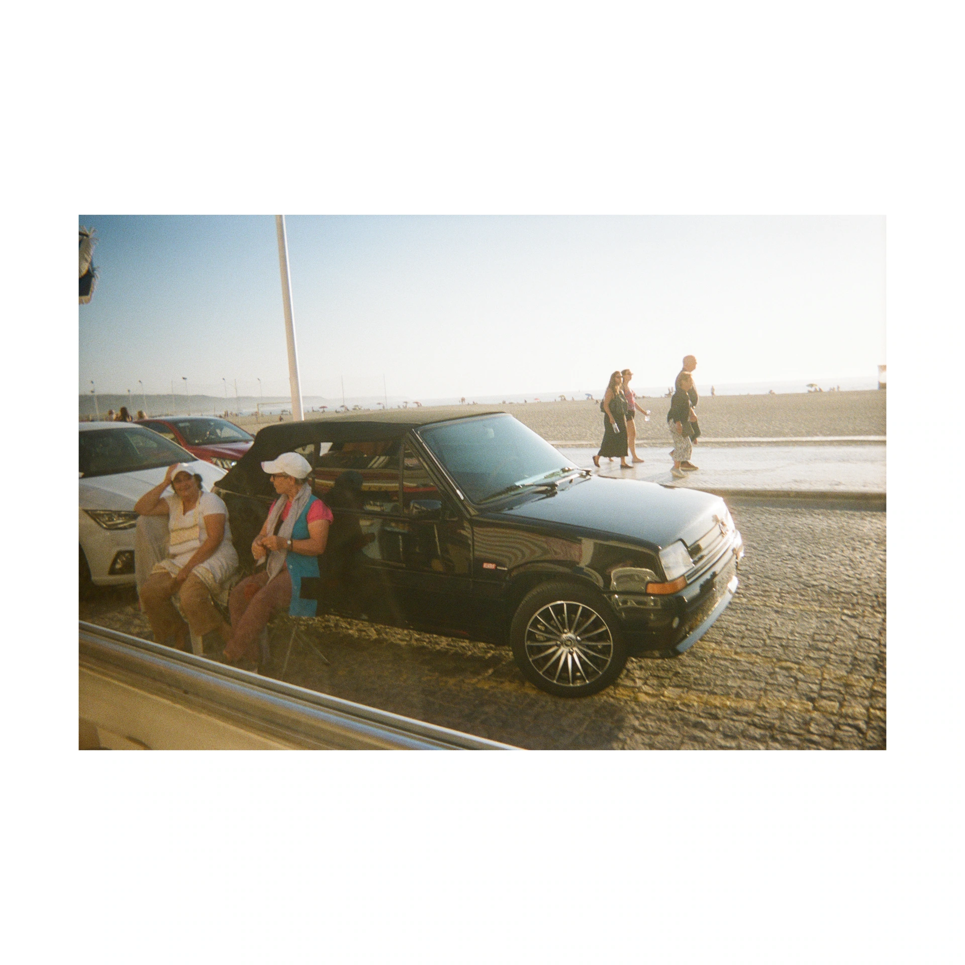 Two people beside a black car on a sunlit promenade