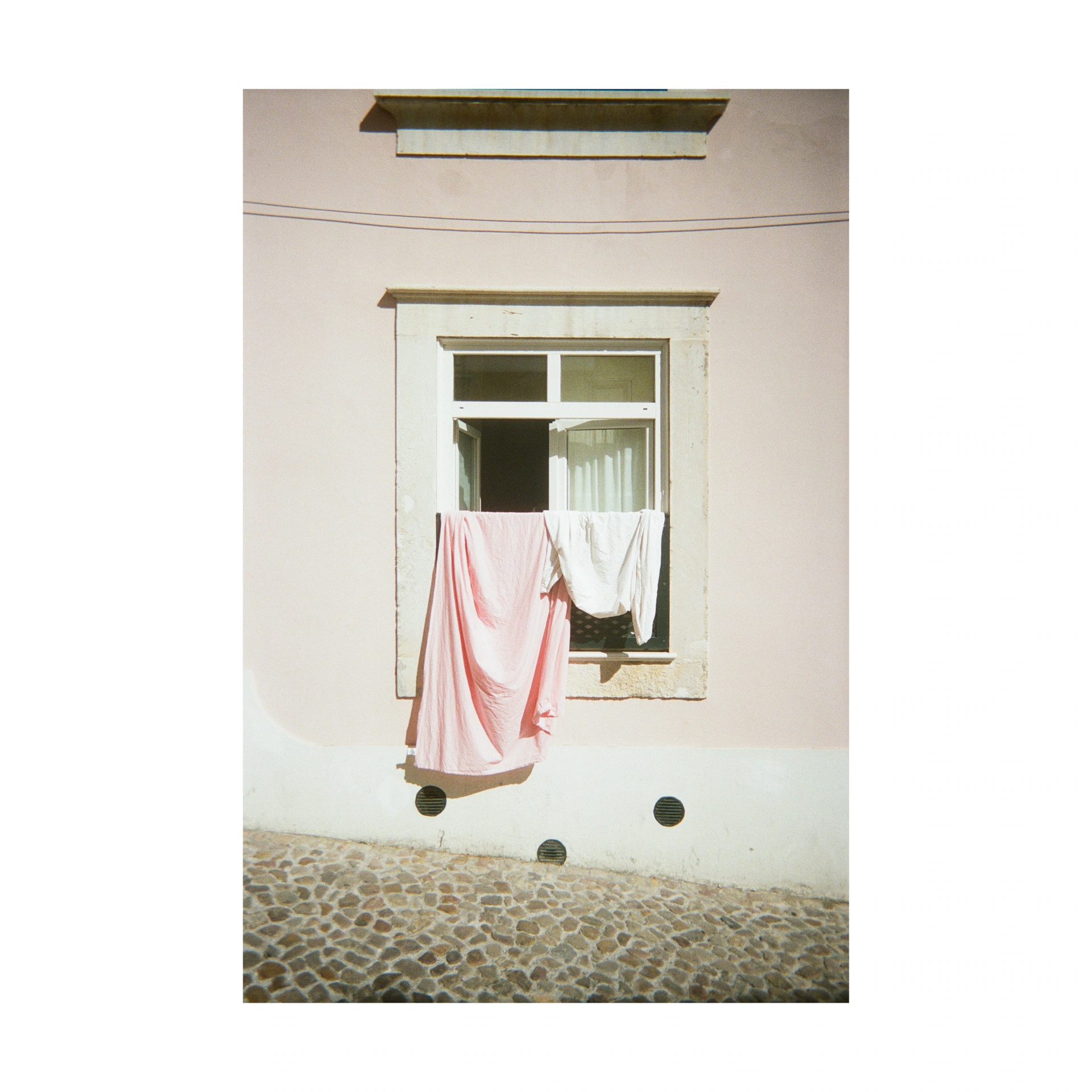 Pink and white laundry hanging from a window above a cobbled street
